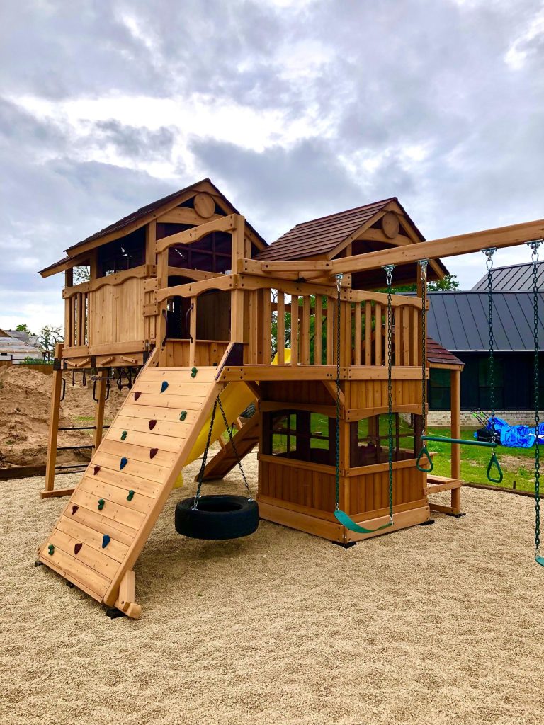 Two-tower cedar playset with a rock wall and yellow slide installed on a gravel base