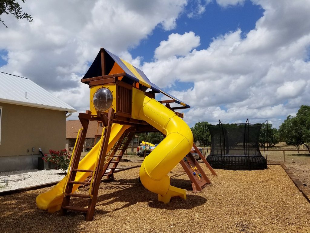 Playset with two yellow slides and a striped canopy installed on a mulch play area