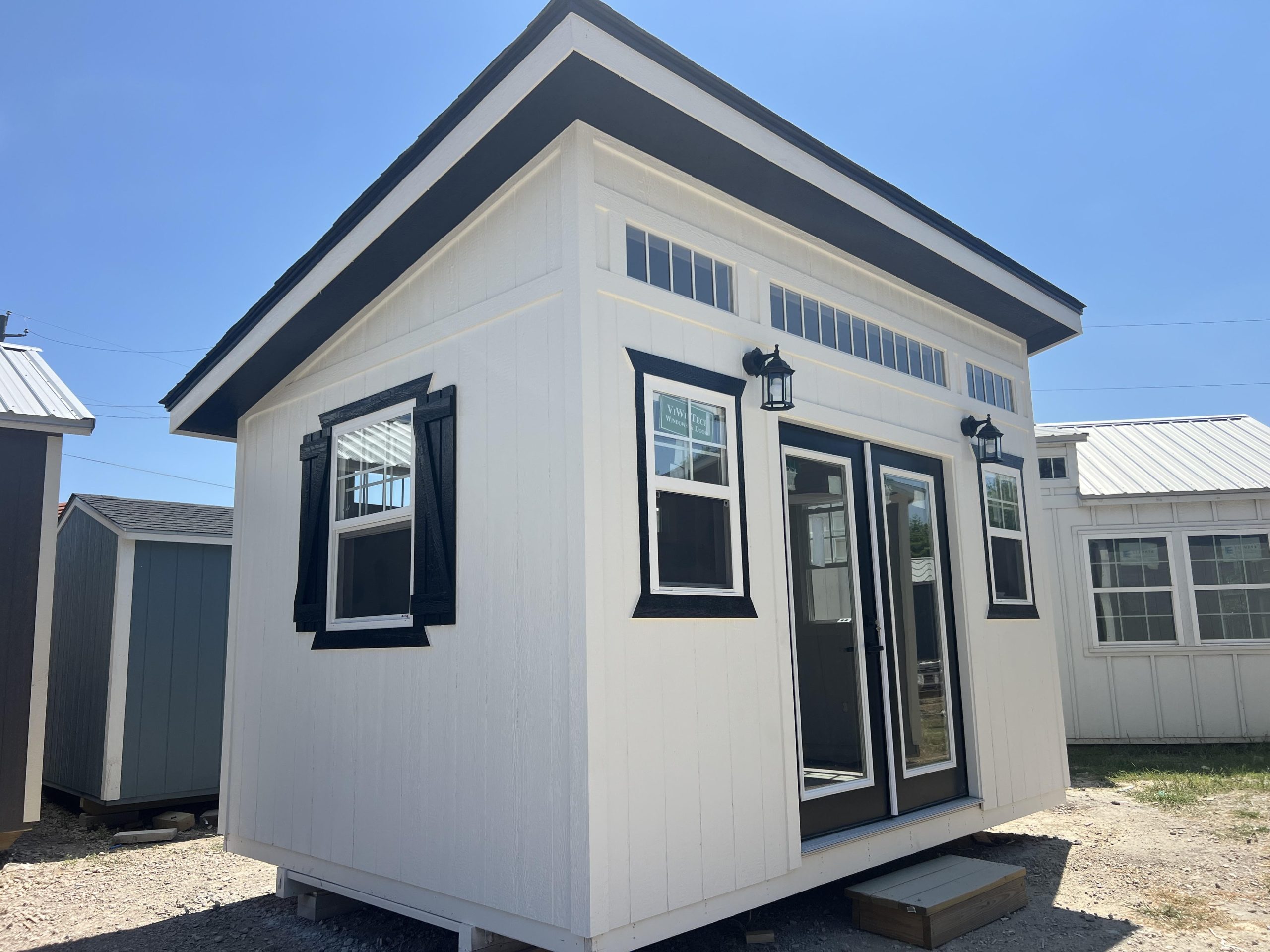 Studio Shed with white siding, black trim, a glazed door, and transom windows