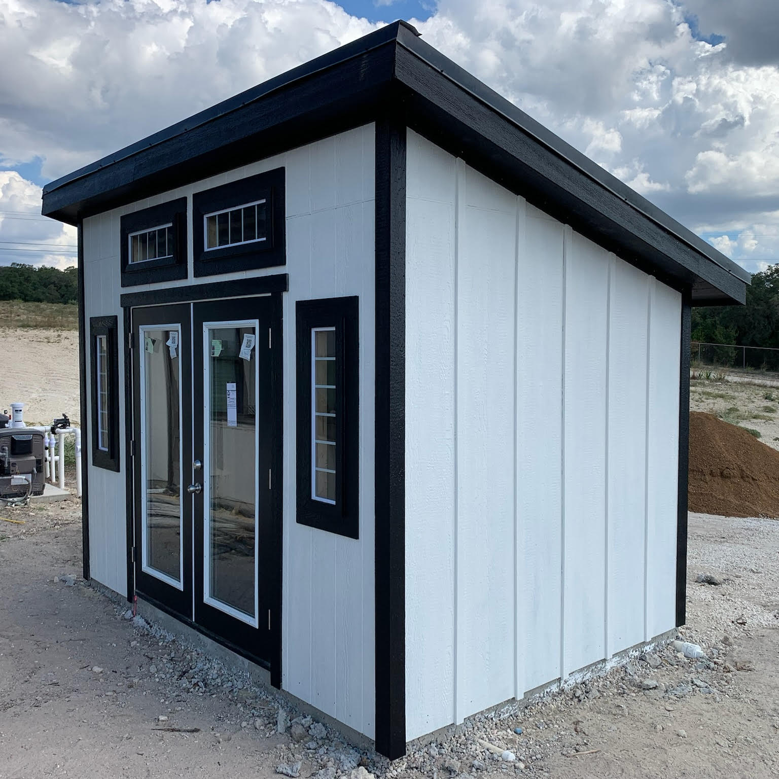Studio Shed with white vertical siding and dark framed glass doors