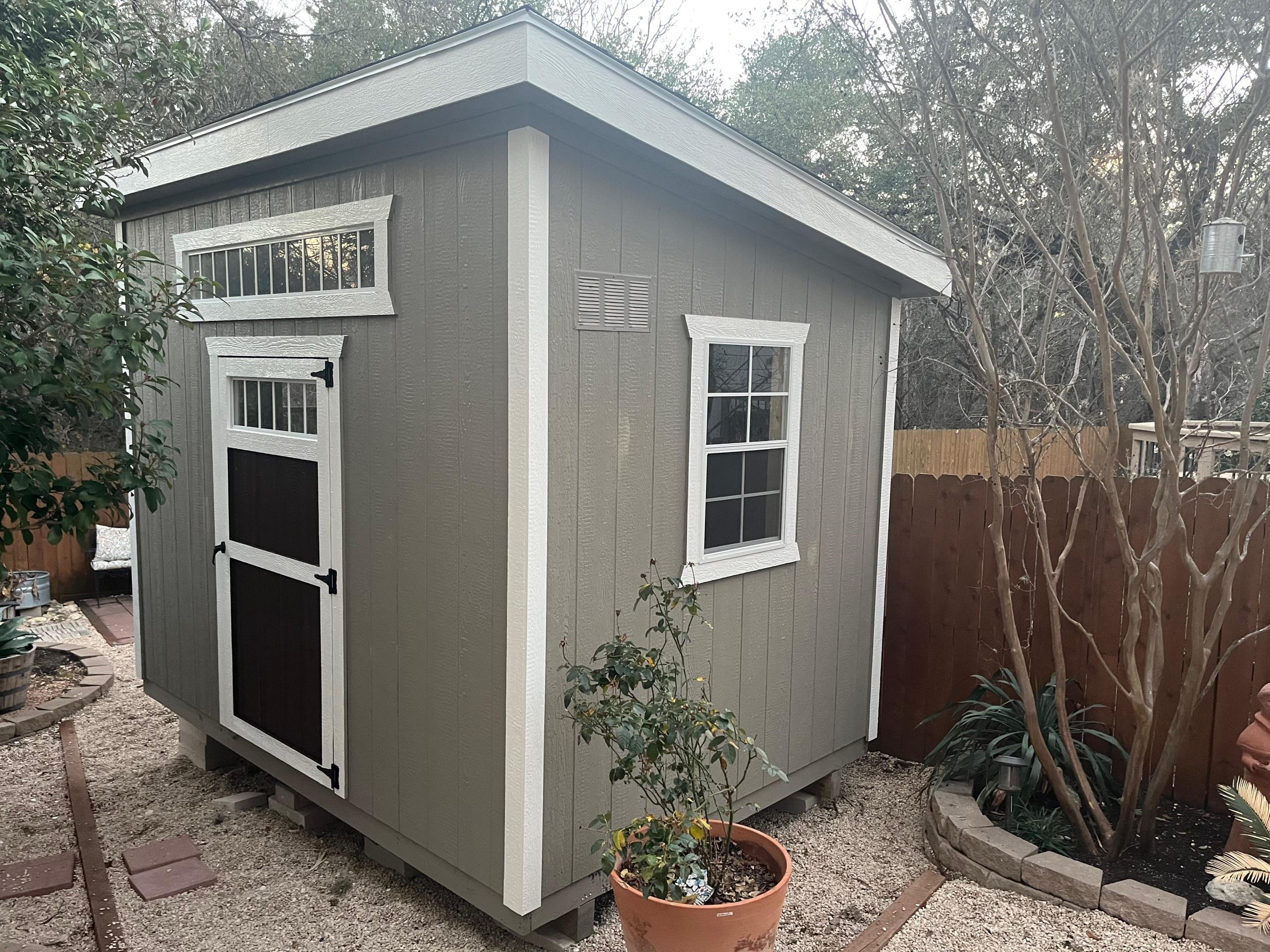 Gray Studio Shed with white trim, a side window, and brown door